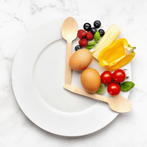 Plate as a clock divided into 16/8 by cutlery, food shown in 8-hour section, representing intermittent fasting